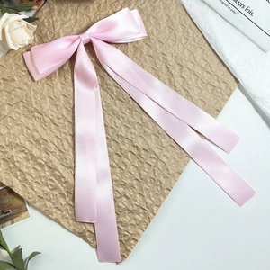 Detail view of pink satin bow hair clip with long ribbons on a decorative background
