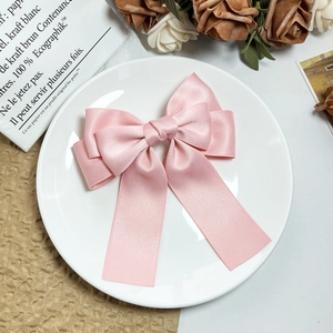 Detail of a pink satin multi-layer bow hair clip with long ribbons in a gift setting
