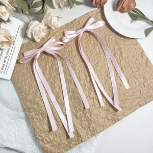 Elegant pair of pink satin bow hair clips with long streaming ribbons on a rustic background
