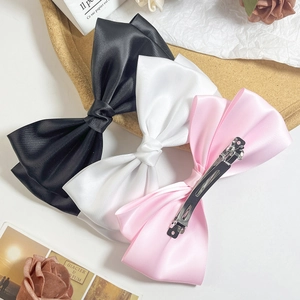 Three large satin bow hair clips in black, white, and pink with metal spring clips
