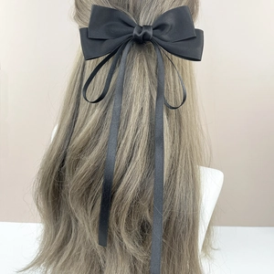 Barrette élégante en satin noir avec grand nœud et longs rubans sur cheveux blonds