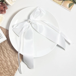 Détail macro du nœud en satin blanc avec perle sur une assiette décorative vintage