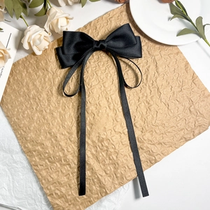 Détail d'une pince à cheveux élégante en satin noir avec double nœud et longs rubans