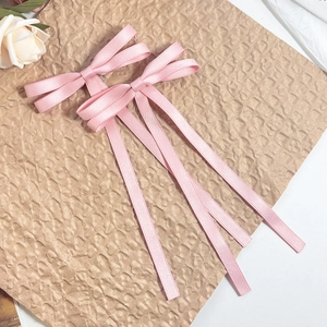 Detailed view of pink satin bow hair clips with long ribbons on textured brown paper