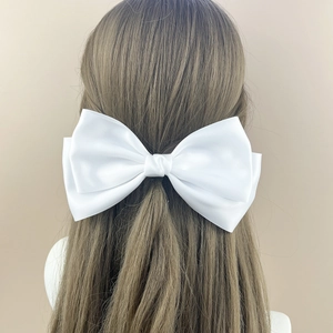 Detailed back view of a large white satin bow hair clip on long brown hair model