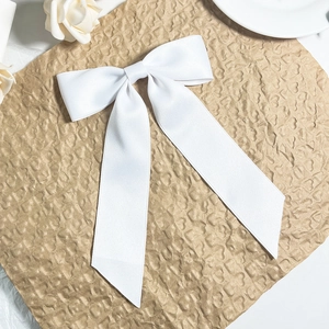 Detail of white satin silk bow hair clip with long ribbons on textured paper background