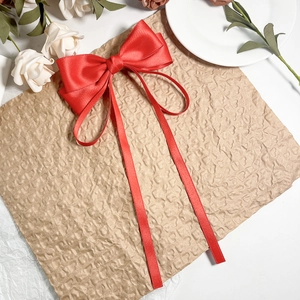 Détail d'une barrette à nœud en satin rouge avec de longs rubans sur papier