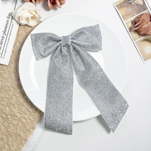 Grosse pince à cheveux nœud argenté à paillettes sur une assiette en porcelaine