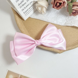 Detailed macro view of a large pink satin bow hair clip with glossy silk texture