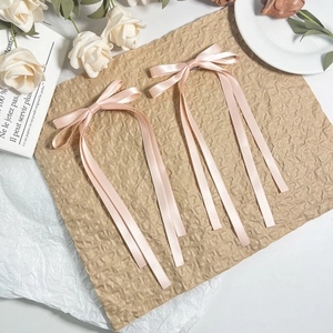 Macro view of soft pink satin ribbon bow hair clips with elegant long streaming tassels