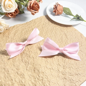 Dettaglio dei fermagli per capelli in raso rosa su sfondo estetico con rose bianche