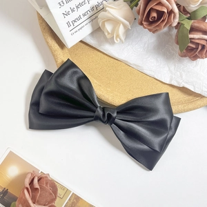 Macro view of the elegant black satin double-layered bow hair clip with glossy silk finish