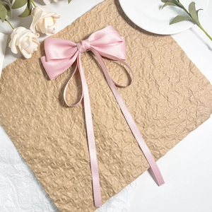 Détail de la pince à cheveux avec nœud en satin rose et longs rubans sur papier kraft