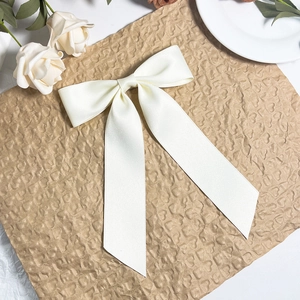 Close-up of elegant cream satin bow hair clip with long ribbons on a decorative floral base
