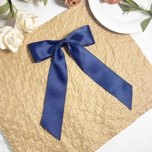 Close-up of a navy blue satin bow hair clip with elegant long ribbon and twill texture
