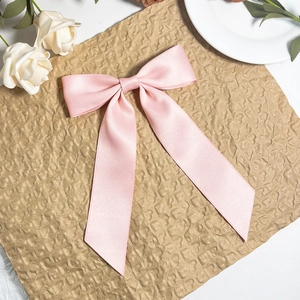 Detail of pink satin bow hair clip with long ribbons on textured paper and rose background