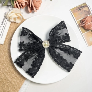 Detail of elegant black hollow lace bow hair clip with pearl center on vintage background