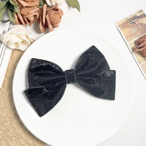 Barrette à cheveux nœud noir scintillant sur une assiette en céramique avec fleurs séchées