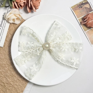 Close-up of lace bow hair clip with central imitation pearl and rhinestone details