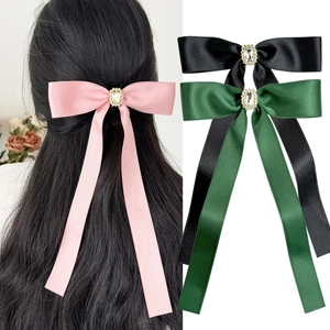 Detailed view of satin bow hair clips with elegant crystals in pink, black, and green colors