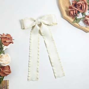 Close-up of cream white bow hair clip with elegant ruffled edges and long fabric ribbons