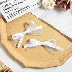 Détail de deux pinces à cheveux avec nœuds blancs en satin et organza sur un plateau