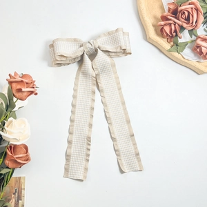 Detail of elegant beige houndstooth bow hair clip with long flowing ribbons and soft texture