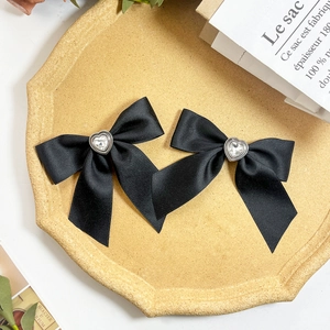 Detail of elegant black satin bow hair clips with heart-shaped crystal center on a tray