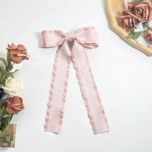 Detail of pink houndstooth bow hair clip with wavy pleated ribbon on white background