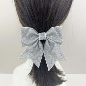 Close-up of a silver glitter bow hairpin with shimmering sequins on dark wavy hair