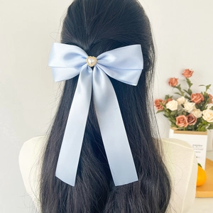 Détail d'un nœud papillon en soie bleu clair avec perle de cœur sur cheveux noirs