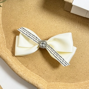 Detailed macro view of cream satin bow hair clip with square crystal and silver diamond trim