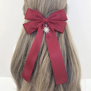 Macro detail of wine red bow hair clip with silver sun pendant and long flowing ribbons