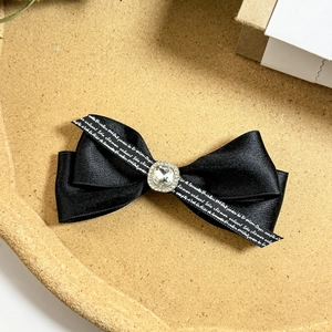 Detailed macro view of black satin bow hair clip with crystal center and white text