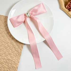 Detail of pink satin bow hair clip featuring a large crystal center and long silk ribbons