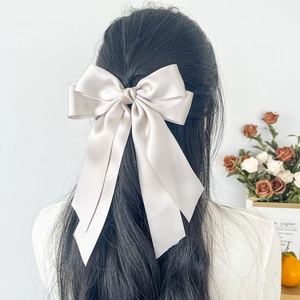 Elegant champagne satin bow hair clip with long ribbons shown on model's back hairstyle
