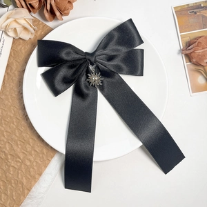 Detail of black satin bow hair clip with a vintage metal sun pendant and long ribbon tails