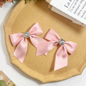 Detail of pink satin bow hair clips with heart-shaped rhinestones on a textured tray