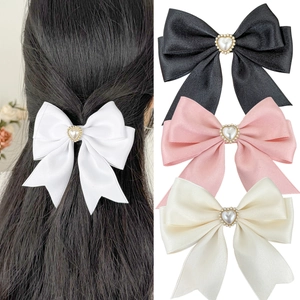 Detailed view of satin bow hair clips with heart-shaped pearls and rhinestone edges