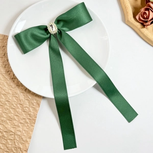 Detailed macro view of dark green satin bow hair clip with central crystal ornament