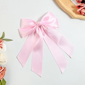 Close-up of pink satin bow hair clip with long ribbons on a minimalist background