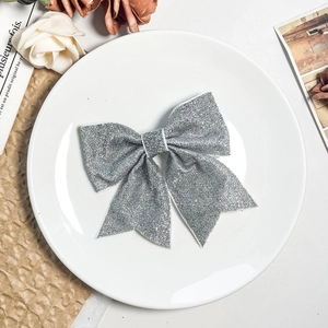 Elegant silver glitter bow hair clip placed on a white ceramic plate with a rose décor