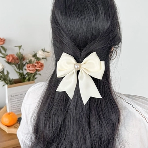 Elegant cream satin bow hair clip with heart pearl center worn on a model's dark hair