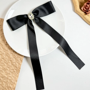 Detail of black satin ribbon bow with large crystal rhinestone in white ceramic dish