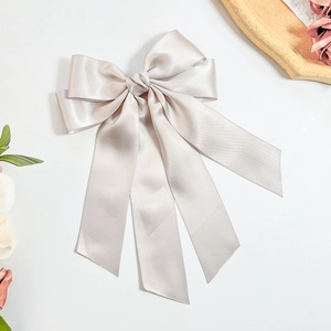 Detailed view of champagne satin bow hair clip with elegant long draping ribbons