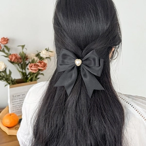 Detail of a black satin bow hair clip with heart pearl worn on half-up black hair