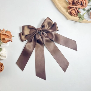 Macro shot of large dark brown satin ribbon bow hair clip with silky flowing streamers