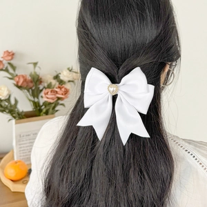 Detail showing a white satin bow hair clip with heart pearl accent worn on a model's hair
