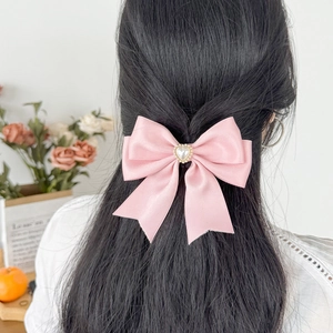 Pink satin bow hair clip with heart pearl on back of model hair in soft natural light