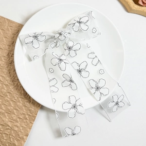 Dettaglio del fiocco in pizzo bianco con motivi floreali neri su tessuto organza